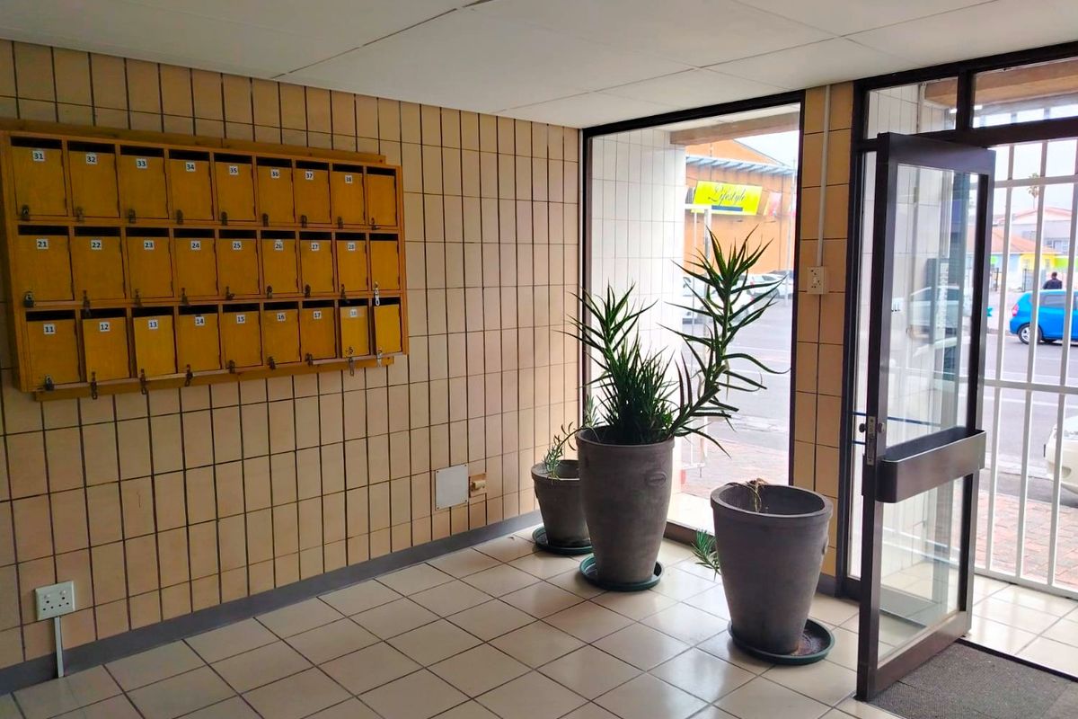Apartment building entrance lobby featuring tiled flooring, wall-mounted mailboxes, and a glass security door leading to the exterior.