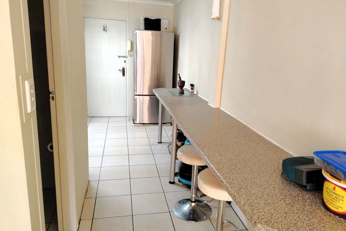 A functional kitchen area featuring a long breakfast bar, tiled flooring, and an integrated intercom system near the entrance.