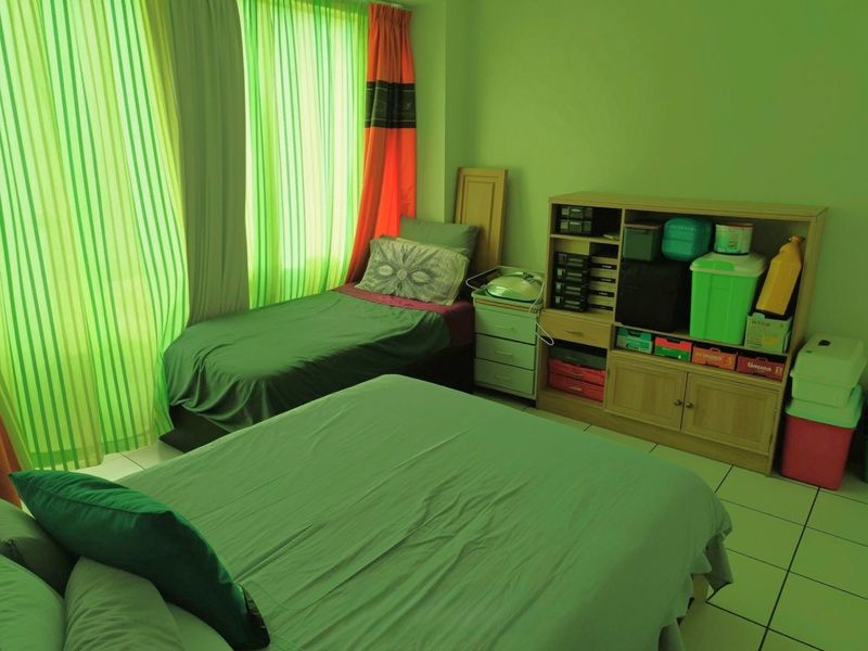 A bedroom featuring tiled flooring and large windows with curtains, providing natural light to the space.