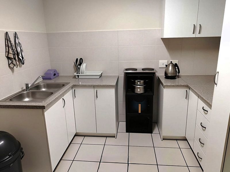 A functional kitchen featuring white cabinetry, laminate countertops, a double bowl stainless steel sink, and a compact electric hob with tiled backsplash.