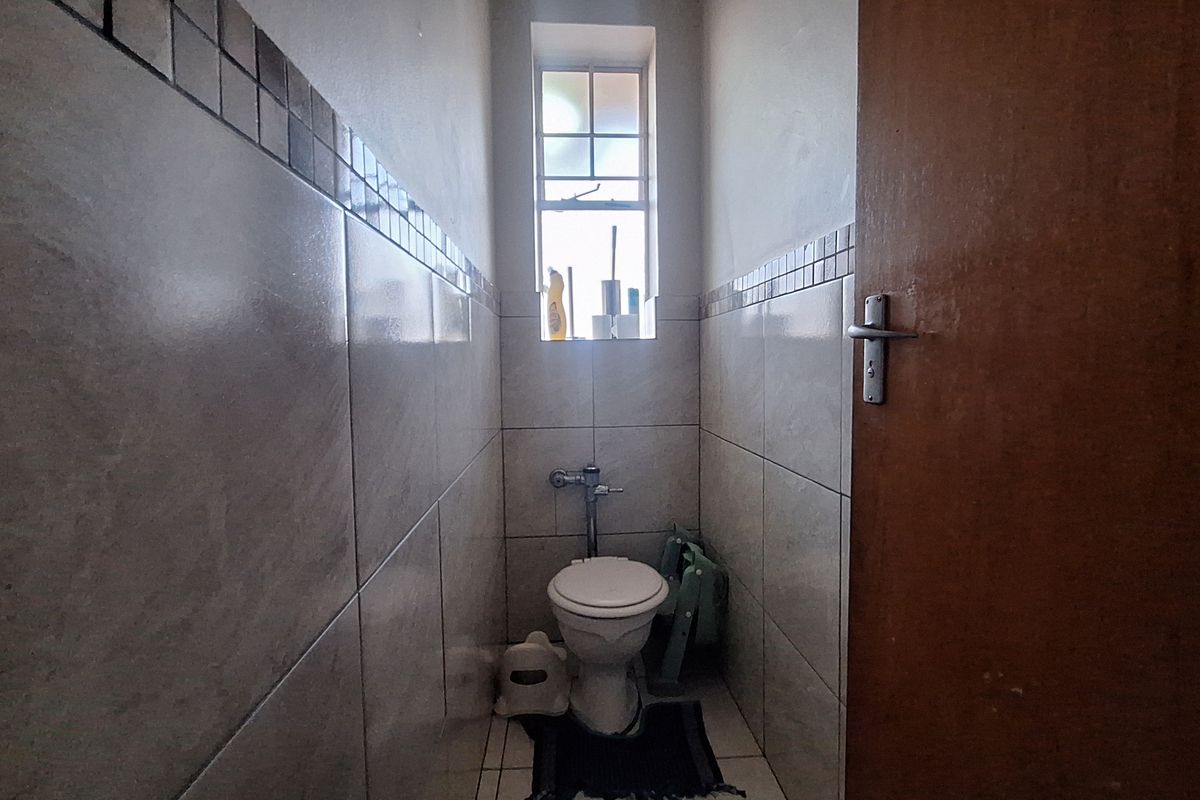 A compact bathroom featuring tiled walls and flooring, a standard toilet, and a window providing natural light.