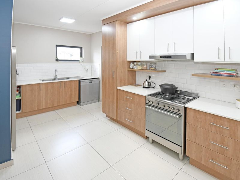 Modern kitchen featuring light wood cabinetry, white subway tile backsplash, gas stove with extractor fan, and tiled flooring.