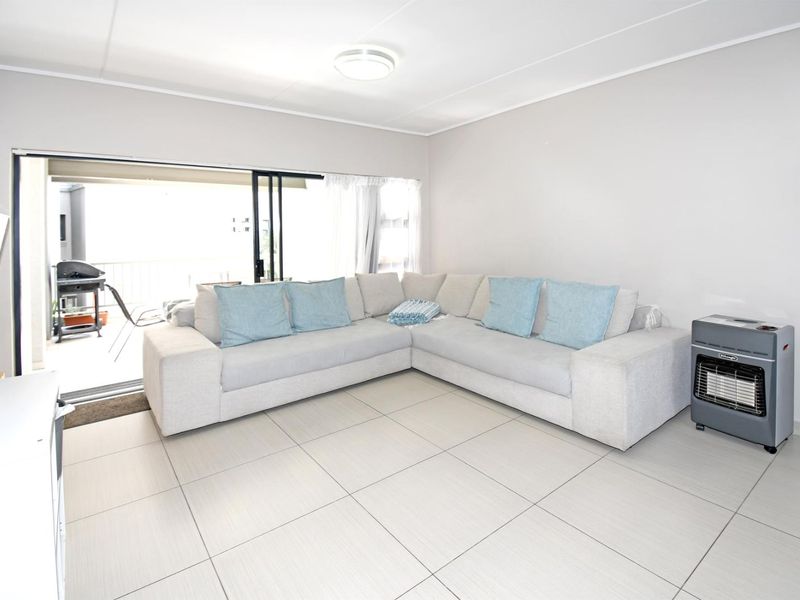 A bright, open-plan living area featuring neutral tiled flooring and a large sliding glass door providing access to the balcony.