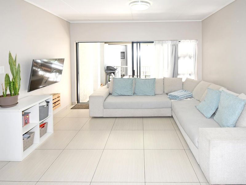 A bright and spacious living room featuring neutral tiled flooring and a large sliding glass door providing access to the outdoor patio area.