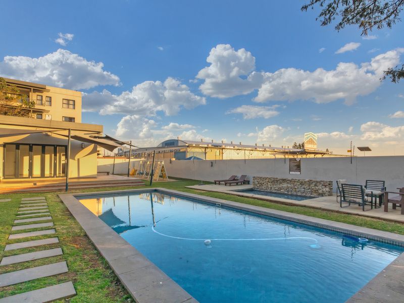 Outdoor pool area featuring a rectangular swimming pool, stone-clad water feature, paved patio space, and a covered terrace attached to the apartment building.