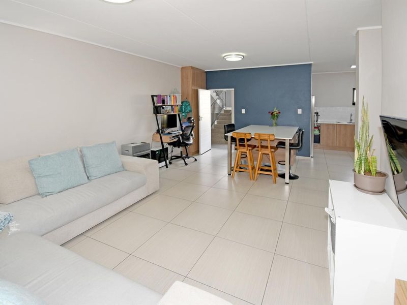 Open-plan living and dining area featuring neutral tiled flooring, a modern kitchen corner, and direct access to an internal staircase.