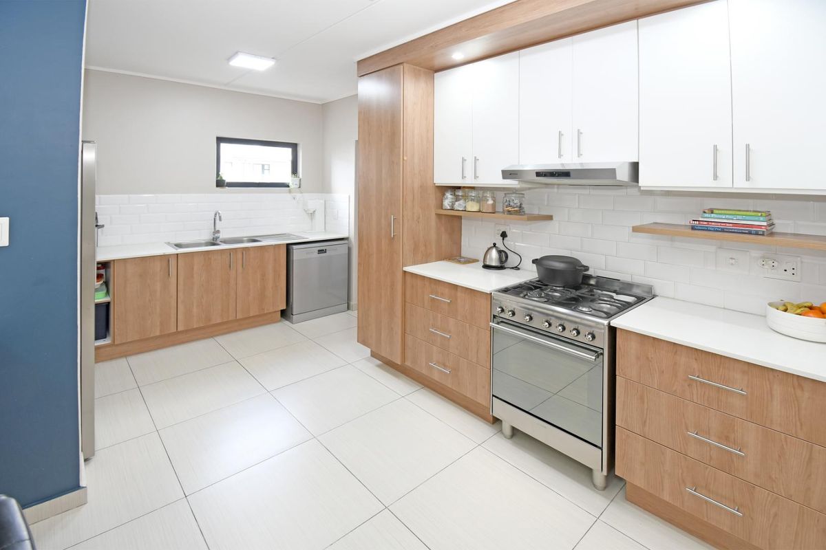 Modern kitchen featuring light wood cabinetry, white subway tile backsplash, gas stove with extractor fan, and tiled flooring.