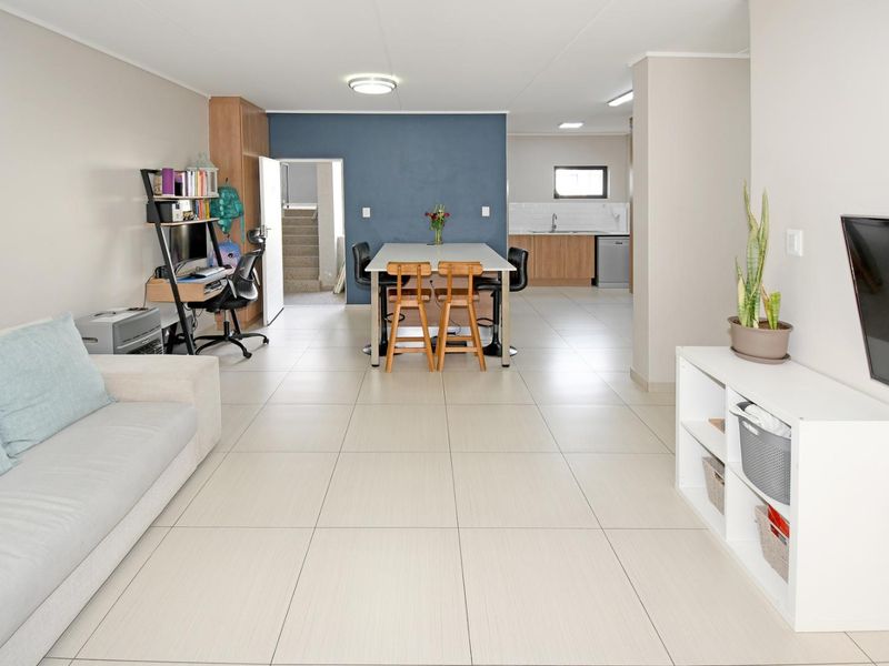 An open-plan living and dining area featuring neutral tiled flooring, a modern kitchen with wood-finish cabinetry, and a distinct blue accent wall.