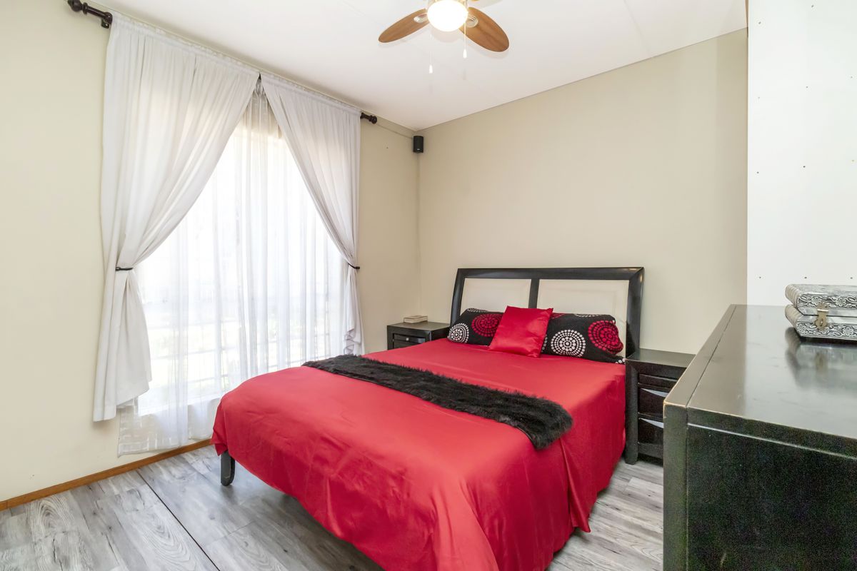 A bedroom featuring light-toned wood-look flooring, a ceiling fan, and a large window with sheer curtains allowing natural light.