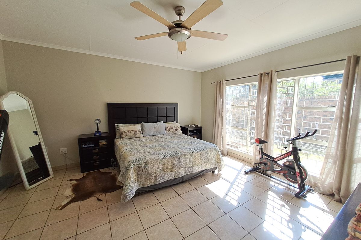 Spacious bedroom featuring tiled flooring, a ceiling fan, and large windows with security bars, providing ample natural light.
