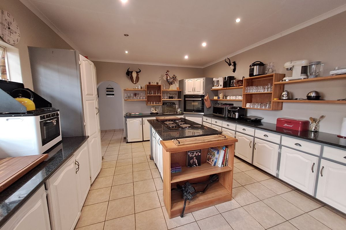 Spacious kitchen featuring a central island with a gas hob, granite countertops, white cabinetry, and open shelving, finished with tiled flooring and recessed lighting.