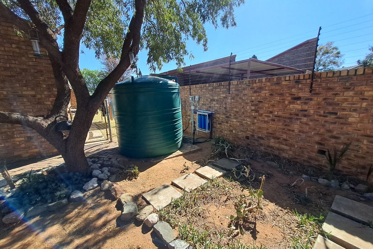 Rear garden area featuring a water storage tank, integrated filtration system, and brick boundary wall with electric fencing.