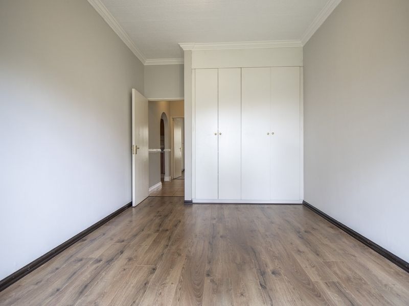 A bright, empty bedroom featuring modern laminate flooring, neutral walls, and built-in cupboards with clean white finishes.