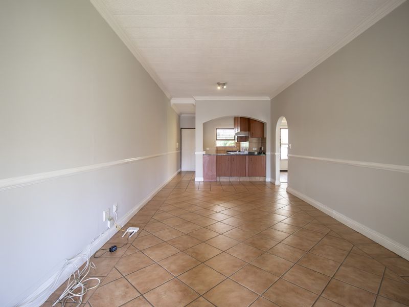 An open-plan living and kitchen area featuring tiled flooring, decorative chair rail molding, and a classic arched entryway leading to the kitchen.