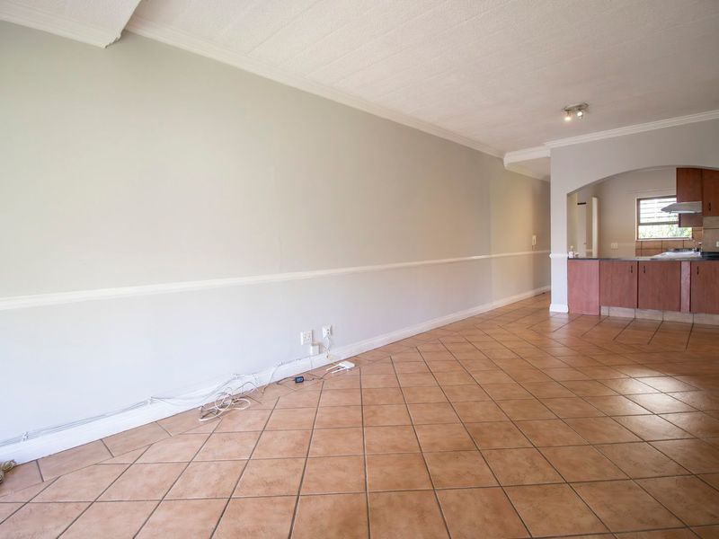 An open-plan living area featuring tiled floors, crown molding, and a connected kitchen with wooden cabinetry and an archway transition.