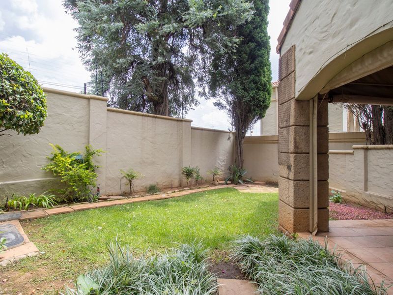 A private rear garden featuring a small lawn, perimeter boundary walls, and a covered tiled patio area with stone pillar detailing.