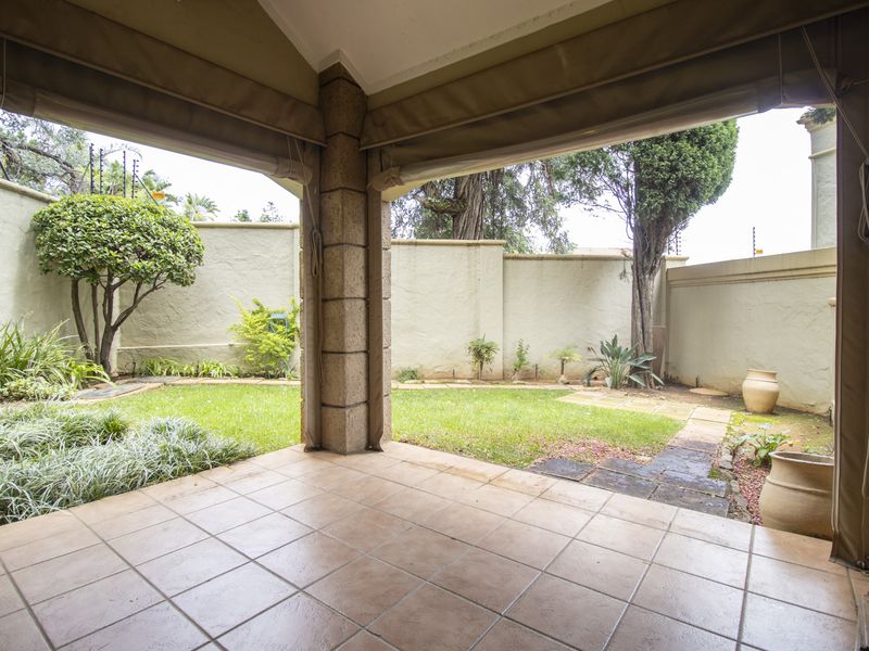 Covered patio featuring tiled flooring and stone-clad pillars, opening onto a private garden with a paved walkway and perimeter boundary wall.