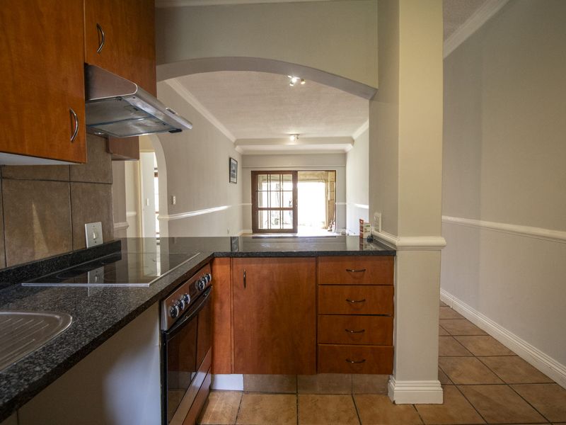 Open plan kitchen featuring wooden cabinetry, granite countertops, and built-in appliances, flowing into a living area with tiled flooring and an arched entryway.