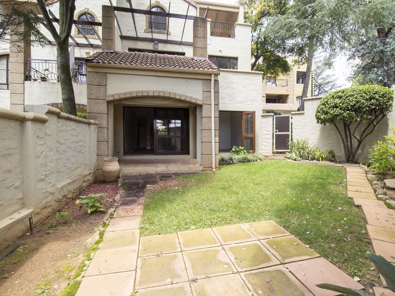 A private rear garden featuring a paved patio area, established lawn, and stone boundary walls, providing direct access to the apartment interior.
