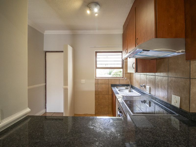 A functional kitchen featuring granite countertops, built-in wooden cabinetry, a stainless steel sink, and an integrated electric hob with an extractor fan.