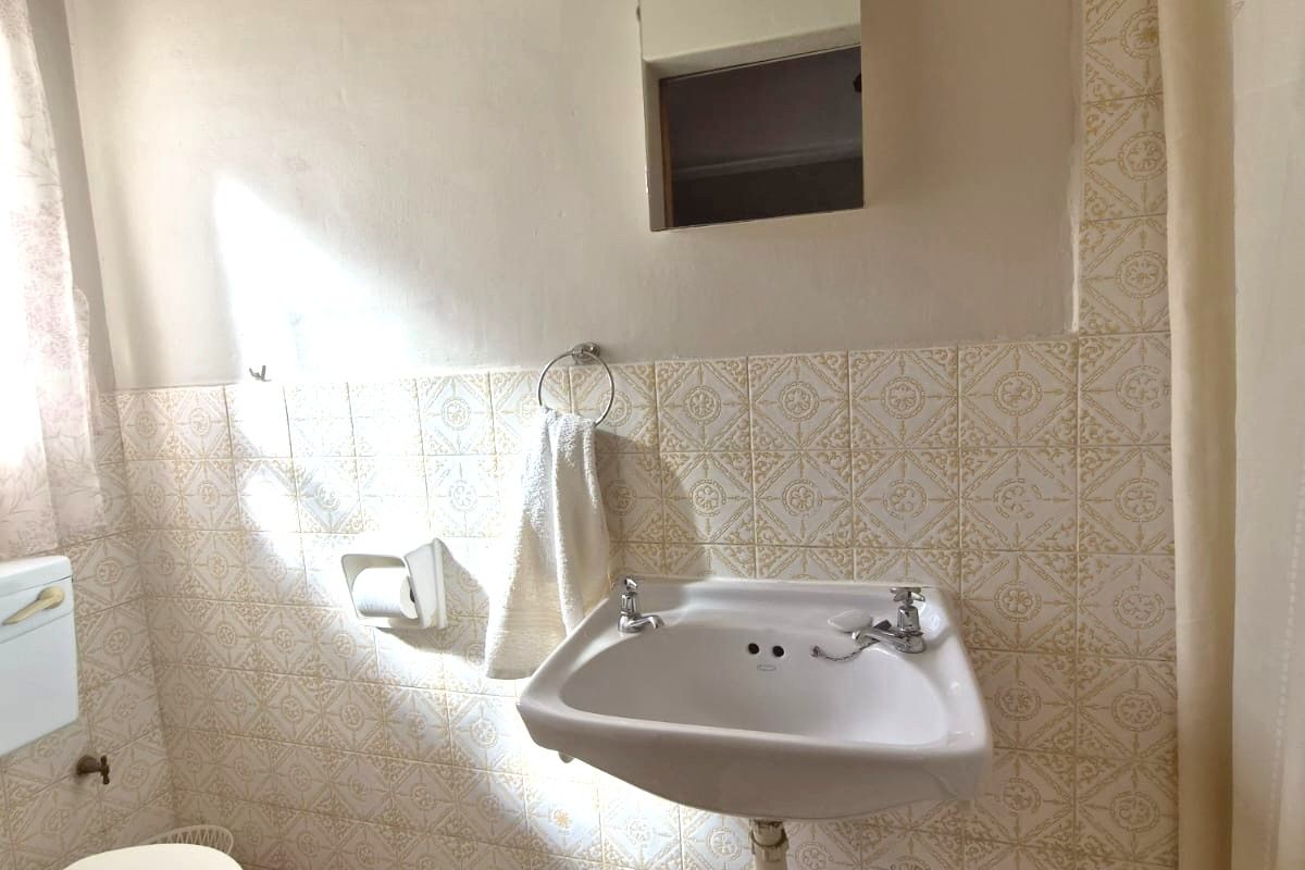 A dated bathroom featuring a wall-mounted basin, toilet, and shower area with vintage patterned wall tiles and flooring.