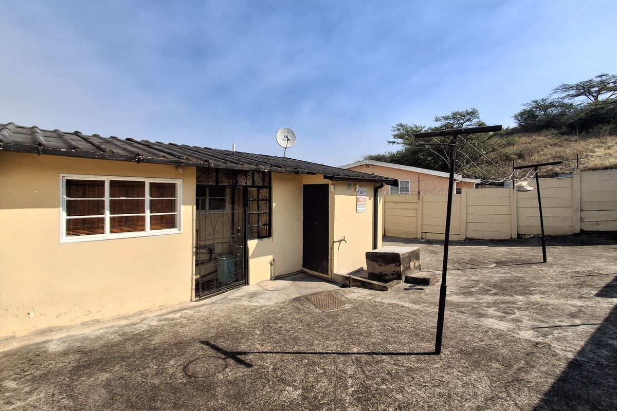 Rear exterior view of the property featuring a paved courtyard, security gate, and outdoor utility area with a concrete wash basin.