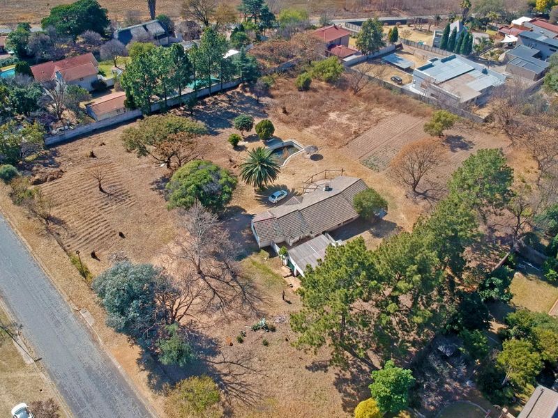 Aerial view of a residential property featuring a large plot, mature landscaping, a swimming pool, and a single-story dwelling with a tiled roof.
