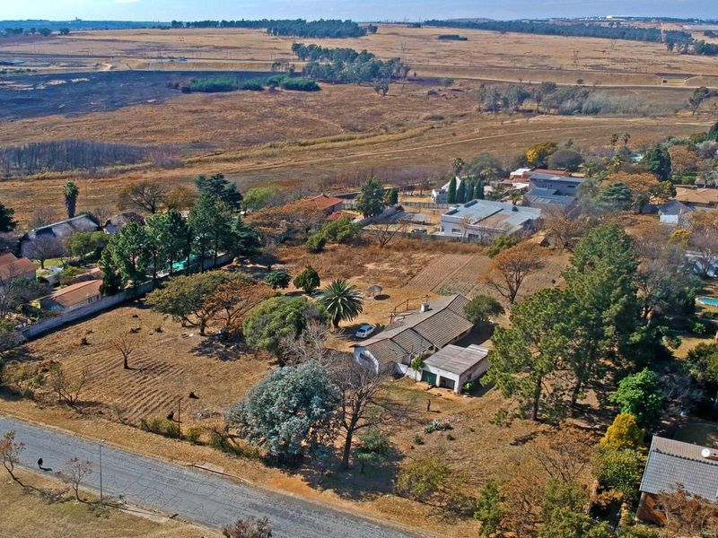Aerial view of a residential property on a large plot featuring mature trees and a single-story dwelling in a suburban setting.