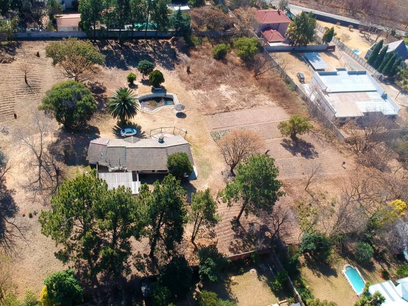 Aerial view of a large residential plot featuring a main dwelling, mature landscaping, and an outdoor swimming pool.