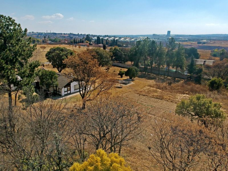 An aerial view of a large residential plot featuring mature trees, open land, and an existing dwelling with a tiled roof.