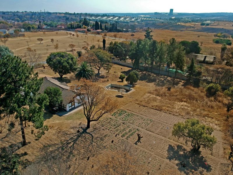Aerial view of a residential plot featuring a dwelling, an unmaintained swimming pool, and expansive dry garden space with mature trees.