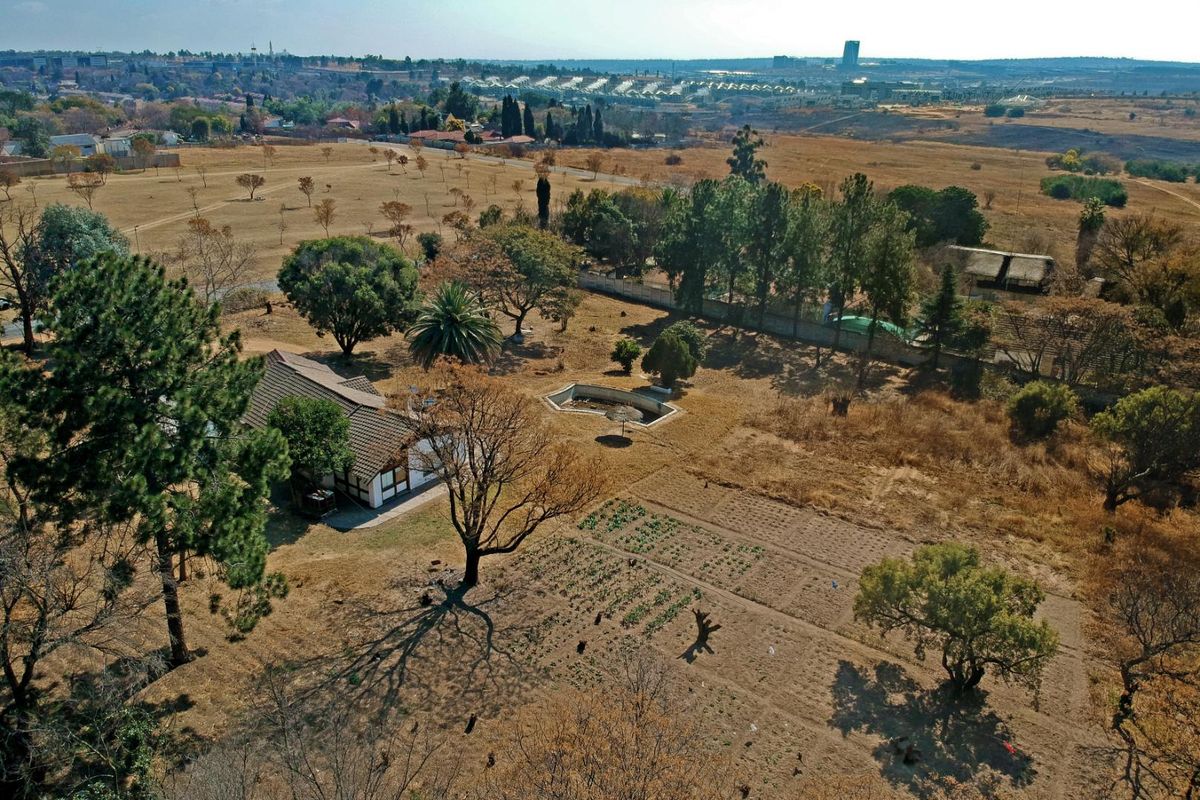 Aerial view of a residential plot featuring a dwelling, an unmaintained swimming pool, and expansive dry garden space with mature trees.