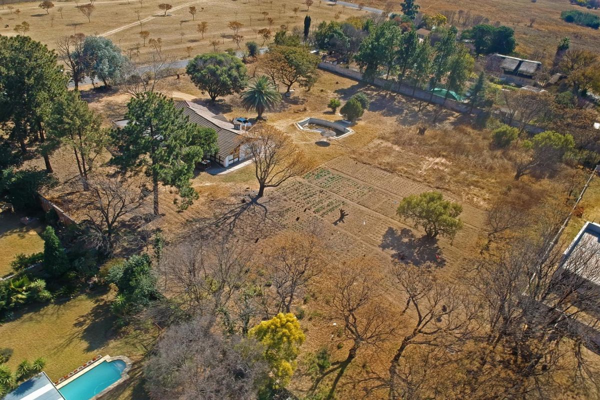 Aerial view of a large residential plot featuring mature trees, a swimming pool, and an established garden area with perimeter fencing.