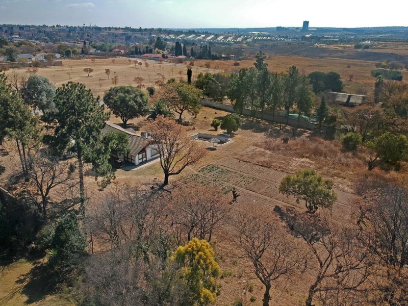 Aerial view of a large residential plot featuring a dwelling, swimming pool, mature trees, and an established garden area within a suburban landscape.