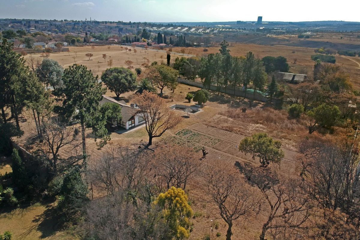 Aerial view of a large residential plot featuring a dwelling, swimming pool, mature trees, and an established garden area within a suburban landscape.