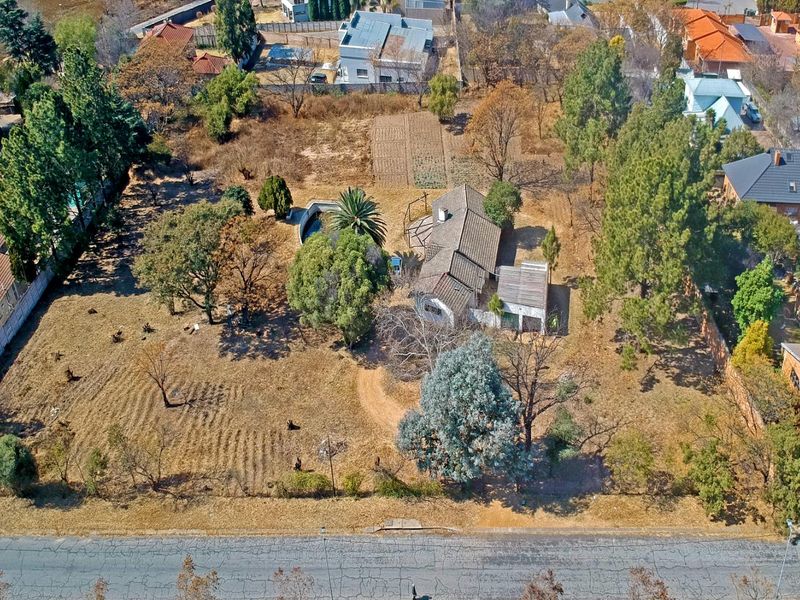 Aerial view of a residential property featuring a large plot with mature trees, a swimming pool, and a single-story dwelling.