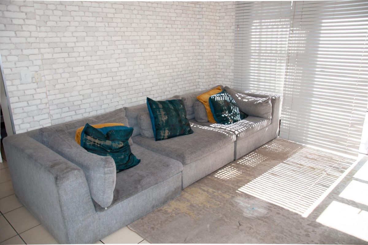 A living room area featuring a textured brick-style feature wall and large window blinds allowing natural light into the space.