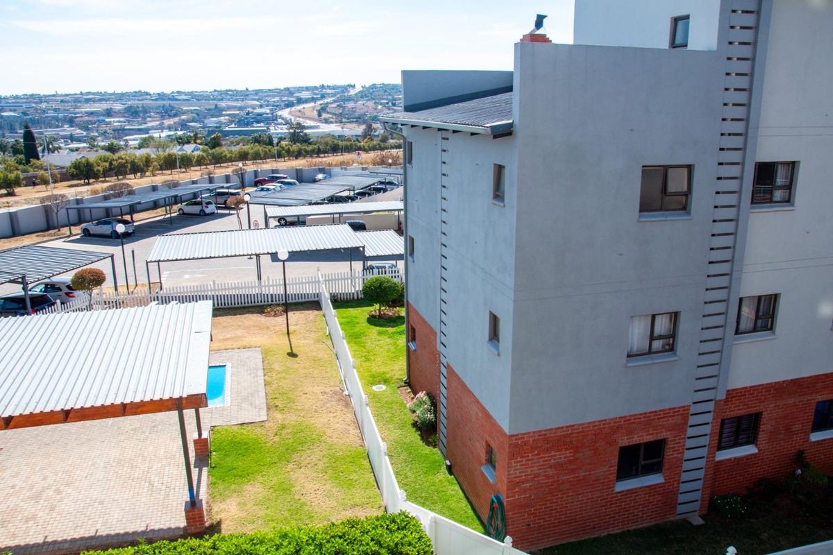 Elevated view of the apartment complex exterior, featuring a brick and plaster facade, communal garden area, and covered parking bays.