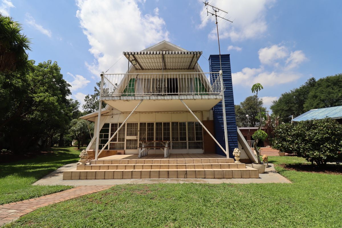 Rear view of an A-frame style small holding residence featuring a raised balcony, tiled patio area, and large glass sliding doors.