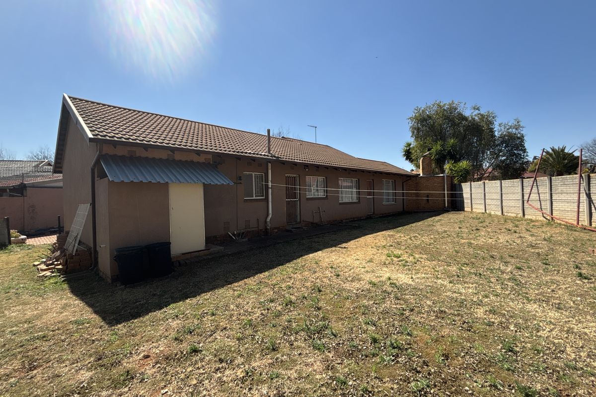 Rear view of the property featuring a tiled roof, concrete perimeter wall, and a spacious backyard area with established boundary fencing.