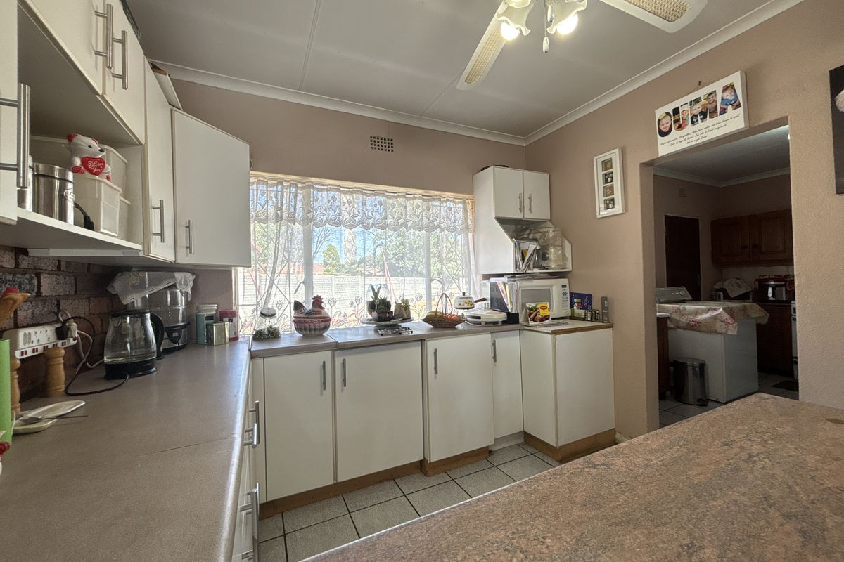 A functional kitchen featuring laminate countertops, built-in cabinetry, and tiled flooring, with an adjacent utility area visible through the doorway.
