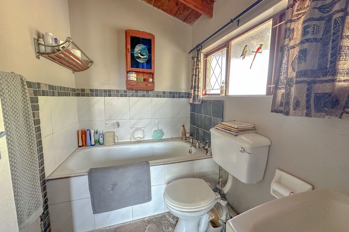 A functional bathroom featuring a built-in bathtub, toilet, and exposed timber ceiling beams, offering a rustic aesthetic with classic tile finishes.