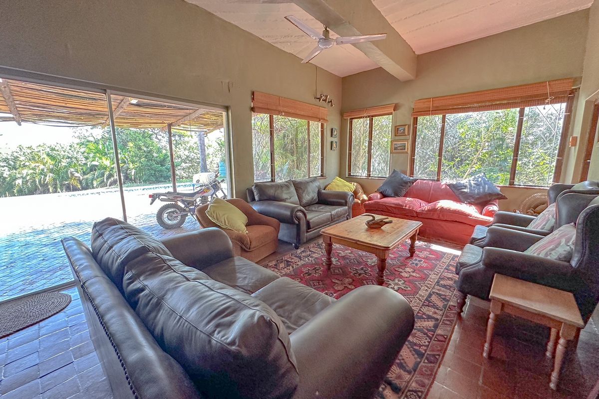 Spacious living room featuring large sliding glass doors, tiled flooring, and exposed beam ceiling, offering direct access to the outdoor patio area.