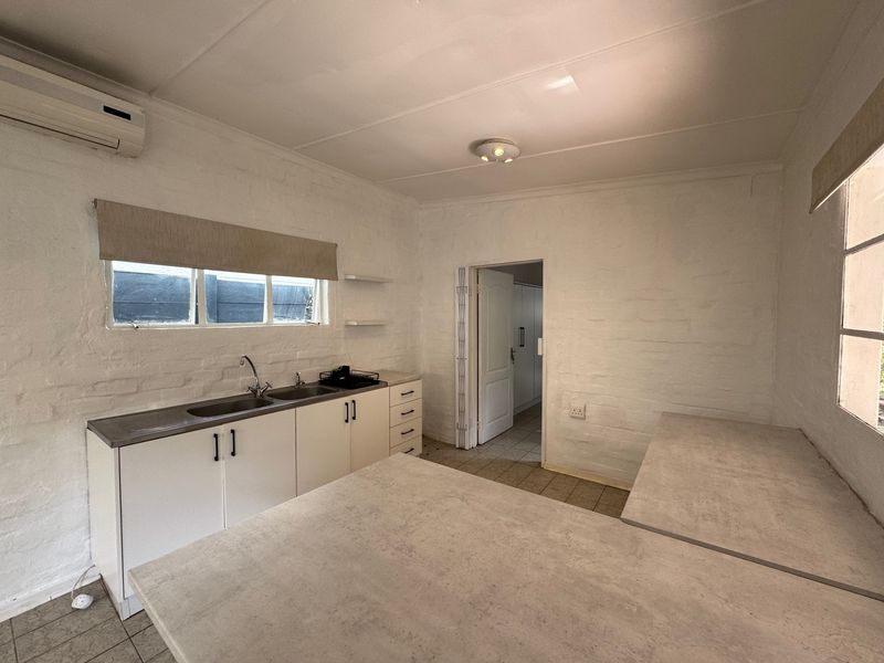 A functional, empty kitchen featuring white painted brick walls, built-in cabinetry, stainless steel sink, and a split-system air conditioner.