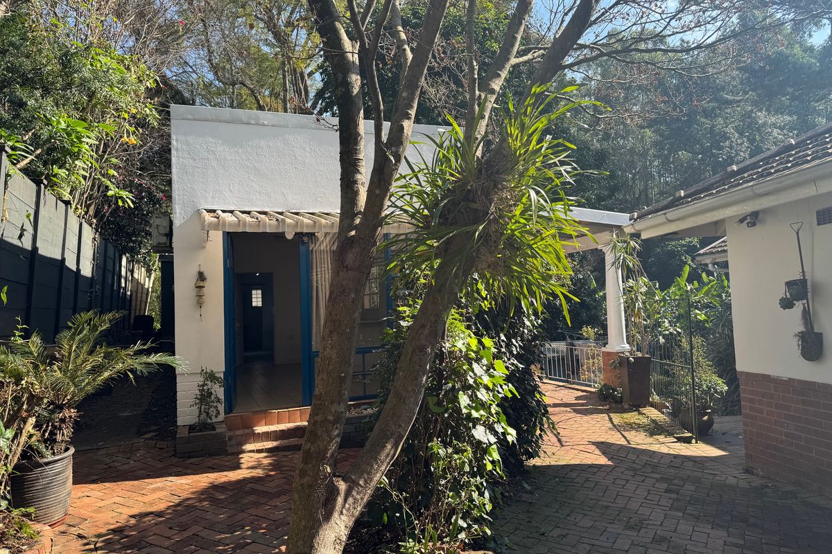 A view of the rear courtyard featuring brick paving, a covered patio area, and access to the cottage structure.