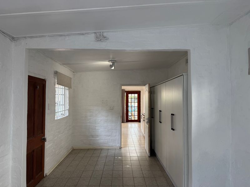 A bright, empty hallway featuring tiled flooring, white-painted exposed brick walls, and built-in storage cabinetry, leading through to an adjacent room with a glass door.