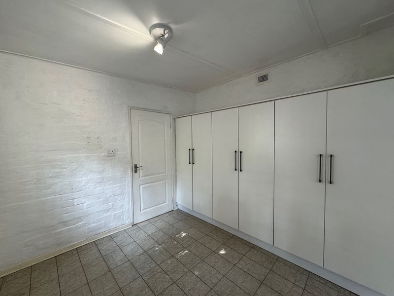 A clean, empty bedroom featuring built-in white cupboards, tiled flooring, and a painted brick wall, offering a neutral canvas for personalization.