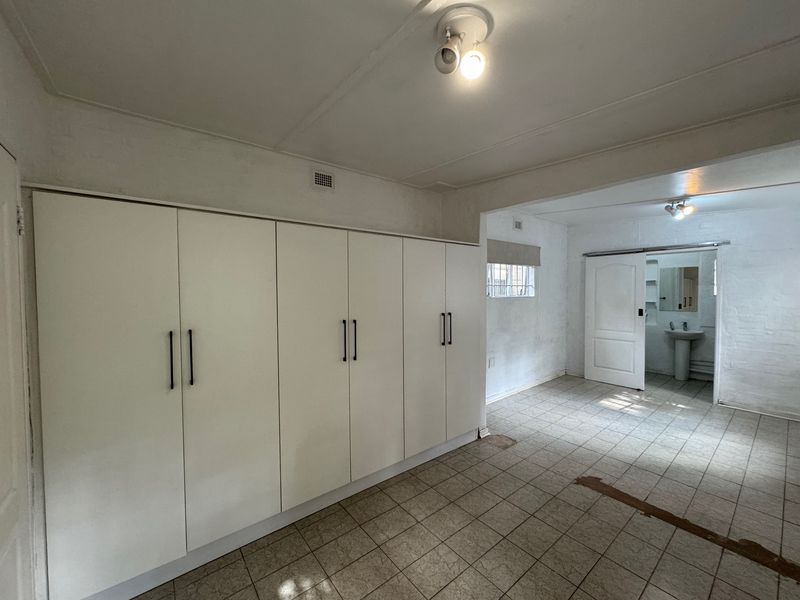 An empty bedroom featuring extensive built-in cupboards, tiled flooring, and an en-suite bathroom area with a pedestal basin.