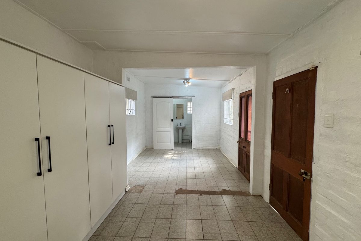 An empty bedroom featuring built-in wardrobes, tiled flooring, and an en-suite pedestal basin area, requiring cosmetic updates to improve its overall condition.