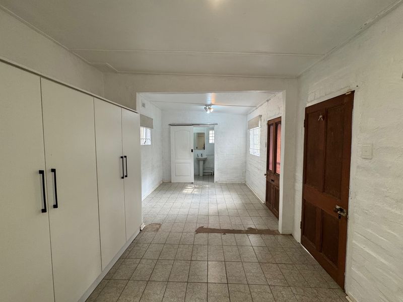 An empty bedroom featuring built-in wardrobes, tiled flooring, and an en-suite pedestal basin area, requiring cosmetic updates to improve its overall condition.